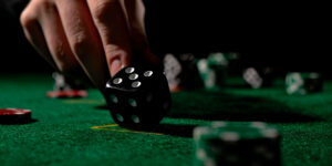 Close up of male hand rolling the dice on green poker table with black background