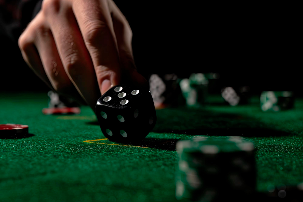 Close up of male hand rolling the dice on green poker table with black background